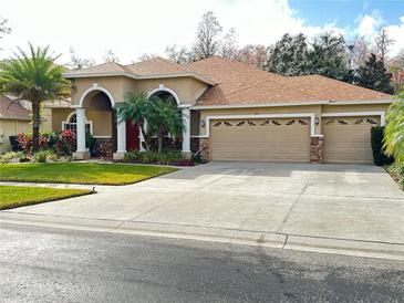 Two-story house with three-car garage, landscaping, and a red door at 3011 Marble Crest Dr, Land O Lakes, FL 34638