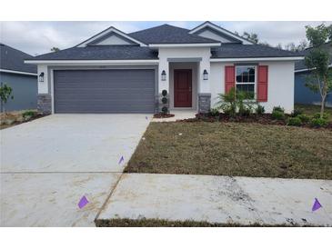 New home exterior featuring gray siding, red shutters, and a two-car garage at 13154 Kent Bradley St, Dade City, FL 33525