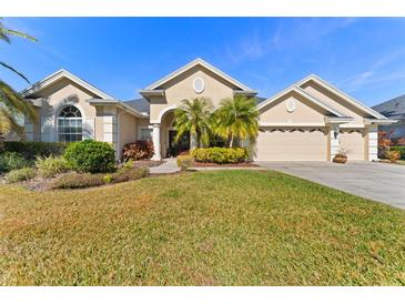 Beautiful tan house with three-car garage, lush landscaping, and palm trees at 26853 Winged Elm Dr, Wesley Chapel, FL 33544