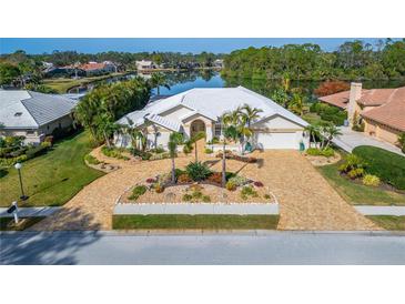 Stunning waterfront home featuring lush landscaping, a brick driveway, and a pristine white tile roof at 7566 Links Ct, Sarasota, FL 34243