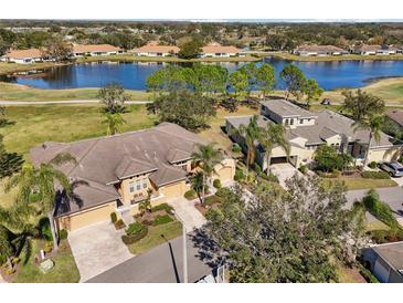 An aerial view shows a tan home with a manicured lawn next to a blue lake in a golf course community at 2471 Kensington Greens Dr, Sun City Center, FL 33573