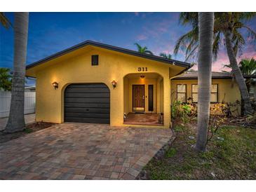 Front view of a yellow house with a dark garage door, and a brick driveway at 311 15Th Ave, Indian Rocks Beach, FL 33785