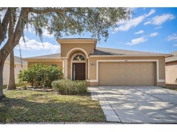 Inviting single-story home featuring a two-car garage, well-manicured landscaping, and a classic arched entryway at 2811 Butterfly Landing Dr, Land O Lakes, FL 34638