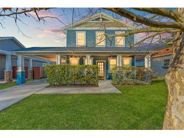 Charming blue two-story home with covered porch, manicured lawn, and mature hedges at 1920 E Idlewild Ave, Tampa, FL 33610