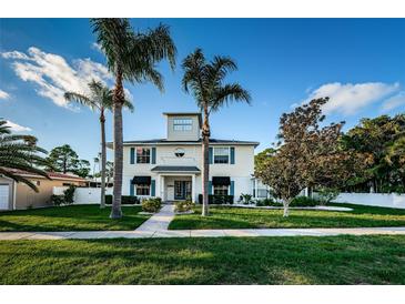 Charming two-story home featuring blue shutters, a manicured lawn, and mature palm trees under a clear blue sky at 614 Maryland Ave, Crystal Beach, FL 34681