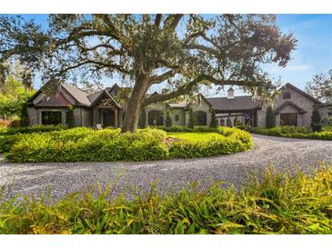 Stately stone home featuring a circular driveway, lush landscaping, and a mature oak tree at 3005 S Miller Rd, Valrico, FL 33596