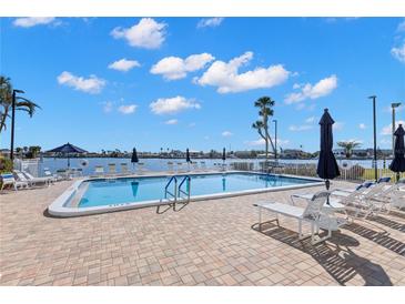 Outdoor pool with lounge chairs overlooking the waterfront on a sunny day with fluffy white clouds at 420 64Th Ave # 402, St Pete Beach, FL 33706