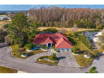 Stunning aerial view of a red-roofed home with lush landscaping, circular driveway and gorgeous surrounding landscape at 5035 Pinelake Rd, Wesley Chapel, FL 33543