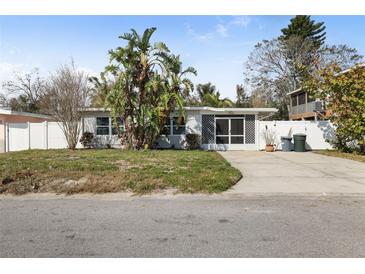 Charming single-story home with tropical landscaping, white picket fence, and a welcoming screened-in porch at 2460 Baywood E Dr, Dunedin, FL 34698