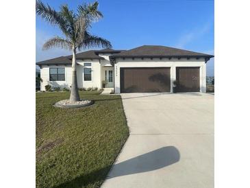 Beautiful new construction home with a three car garage and a well manicured lawn, palm tree and concrete driveway at 15426 Mccomb Cir, Port Charlotte, FL 33981