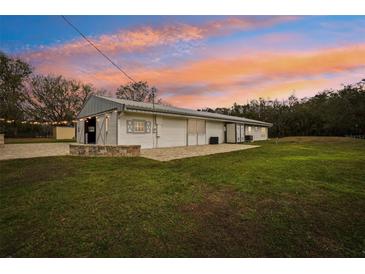 Charming white home featuring large doors, a metal roof, and a spacious green lawn under a beautiful sunset sky at 2040 Underwood Ln, Zephyrhills, FL 33540
