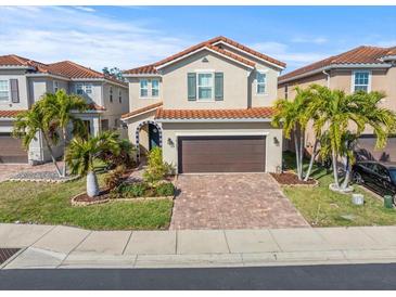 Charming two-story home with a well-manicured lawn, brick driveway, and a red tile roof at 10193 Grand Oak Cir, Madeira Beach, FL 33708