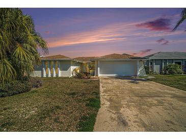 A single-story home at dusk with two-car garage, manicured lawn and mature landscaping provides a welcoming curb appeal at 13614 Evelane Dr, Hudson, FL 34667