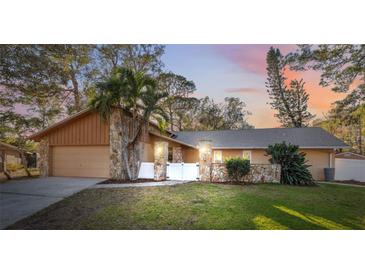 Charming home featuring a well-manicured lawn and a stone pillar-accented facade, all bathed in the warm glow of the setting sun at 3092 Osprey Ln, Clearwater, FL 33762