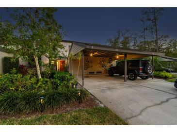 Charming home exterior with covered parking, lush landscaping, and inviting red front door at twilight at 110 Woods Landing Trl, Oldsmar, FL 34677