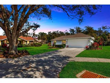 Charming single-story home with lush lawn, mature tree, and two-car garage, bathed in warm light at 37157 Foxrun Pl, Zephyrhills, FL 33542