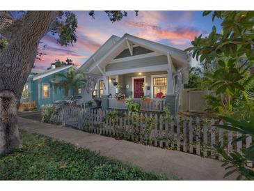 Charming home featuring a picket fence, lush landscaping, and a cozy front porch with a red front door at 731 7Th N St, St Petersburg, FL 33701