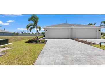 Modern home showcasing a paved driveway leading to a two-car garage with manicured lawn and tropical landscaping at 8069 Shore Lake Dr, Englewood, FL 34224