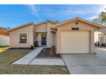 Tan single-story home featuring a one car garage, black door, and a small garden under the window at 1242 Holly Cir, Oldsmar, FL 34677