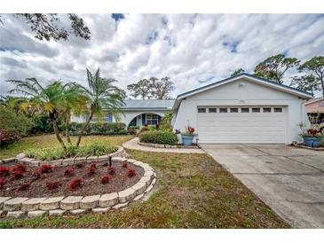 Charming home featuring a two-car garage, blue shutters, and a meticulously landscaped front yard with beautiful flowerbeds at 2086 Whitney N Pl, Clearwater, FL 33760