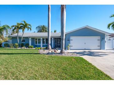 Charming single-story home with manicured lawn, mature palm trees, and a two-car garage at 230 S Julia Cir, St Pete Beach, FL 33706