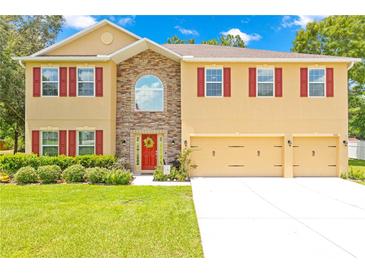 Inviting two-story home featuring a well-manicured lawn and a three-car garage at 5147 Elwood Rd, Spring Hill, FL 34608