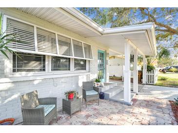 Inviting front porch with cozy seating area, brick flooring, and a turquoise front door at 349 Shirley Ave, Belleair, FL 33756