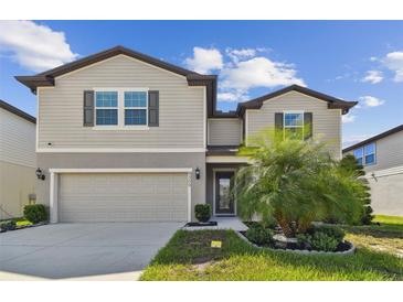 Two-story house with tan siding, two-car garage, and landscaping at 9309 Rally Spring Loop, Wesley Chapel, FL 33545