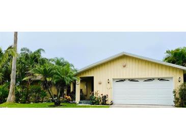 Cute yellow house with white garage door and lush landscaping at 1964 Arvis E Cir, Clearwater, FL 33764