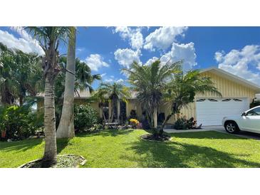 Inviting yellow house with palm trees, a well-manicured lawn, and a two-car garage at 1964 Arvis E Cir, Clearwater, FL 33764