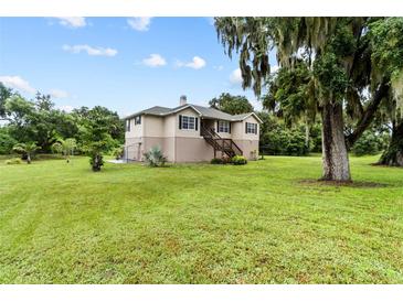 House exterior showcasing a tan home with black shutters, a wooden deck, and a spacious green lawn at 7205 86Th E St, Palmetto, FL 34221