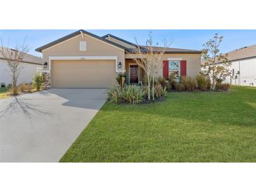 Tan house with red shutters, two-car garage, and landscaped lawn at 12931 Conquistador Loop, Spring Hill, FL 34610