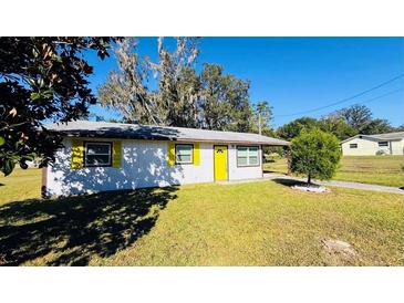 White house with yellow door, brown accents, and a well-maintained lawn at 27299 Azen Loop, Brooksville, FL 34602