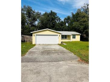 Cute yellow house with a white garage door and a well-maintained lawn at 27173 Simona Ave, Brooksville, FL 34602