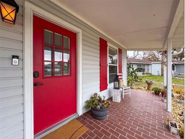 Inviting front porch with red door, brick flooring, and potted plants at 1661 Larkin Rd, Spring Hill, FL 34608