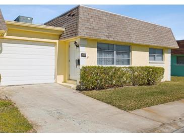 Cute yellow house with a white garage door and well-manicured lawn at 7037 Versailles N # 15, Pinellas Park, FL 33781