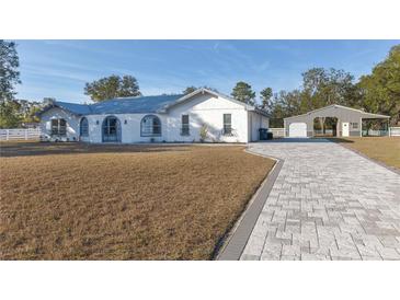 White single-story home with gray roof, paver driveway, and detached barn at 9331 Elida Rd, Spring Hill, FL 34608