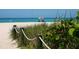 Beach access path with wooden posts and rope, lush vegetation, and ocean view at 100 Sands Point Rd # 305, Longboat Key, FL 34228