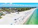 Wide sandy beach with clear blue waters, volleyball nets, beachgoers, lifeguard tower, and lush green trees at 3607 E Bay Dr # 202, Holmes Beach, FL 34217