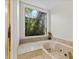 Bright bathroom featuring a soaking tub with marble surround and garden view from a large picture window at 4714 Elder Berry Dr, Sarasota, FL 34241