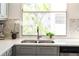 Close-up of a kitchen sink overlooking the window and lush greenery, with stone countertops and grey cabinets at 5174 Marsh Field Ln # 86, Sarasota, FL 34235