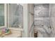 Modern bathroom shower featuring gray tiled walls, a wooden stool, and decorative starfish on the marble countertop at 505 Tamiami N Trl # 201, Venice, FL 34285