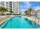 Long swimming pool with nearby lounge furniture and the building behind palm trees against a bright blue sky at 111 S Pineapple Ave # 1018, Sarasota, FL 34236