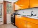 Mid-century kitchen with orange cabinets, stainless steel appliances, and terrazzo floor at 1695 Lowe Dr, Sarasota, FL 34236