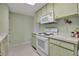 Galley style kitchen with white appliances and light green cabinets at 5708 Miami Rd, Venice, FL 34293