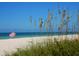 Serene beach scene with a red and white striped umbrella under a clear blue sky at 12317 Baypointe Ter, Cortez, FL 34215