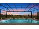 Screened-in pool and spa offer views of the green landscape as the sun sets with a vibrant orange glow at 8376 Sea Glass Ct, Sarasota, FL 34240