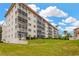 A ground view of the condo's facade featuring screened balconies, green landscaping, and tropical palm trees at 1600 1St W Ave # 304A, Bradenton, FL 34205