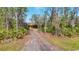 A gravel driveway leads to a charming yellow house nestled among tall trees at 3340 Ulman Ave, North Port, FL 34286