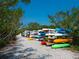 Kayak storage rack along a gravel path with colorful kayaks, shaded by trees against a vibrant blue sky at 1666 Pintail Way # 9, Sarasota, FL 34231